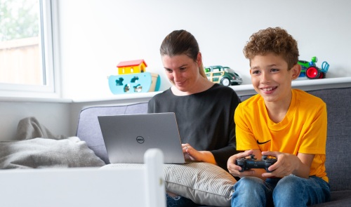 Mum using laptop and son and son playing a game in living room