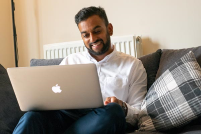 Man in his twenties at home on the sofa on his laptop