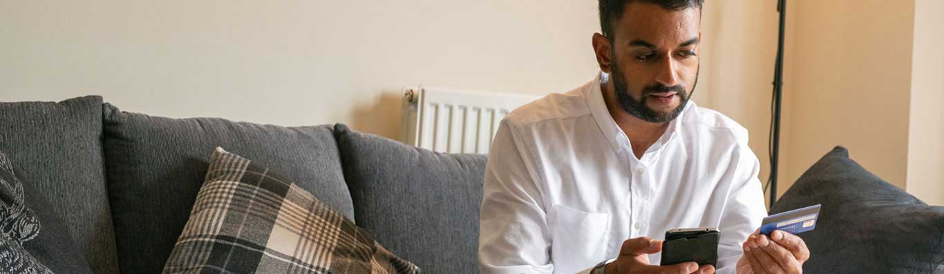 A man looking at his smartphone and his credit card